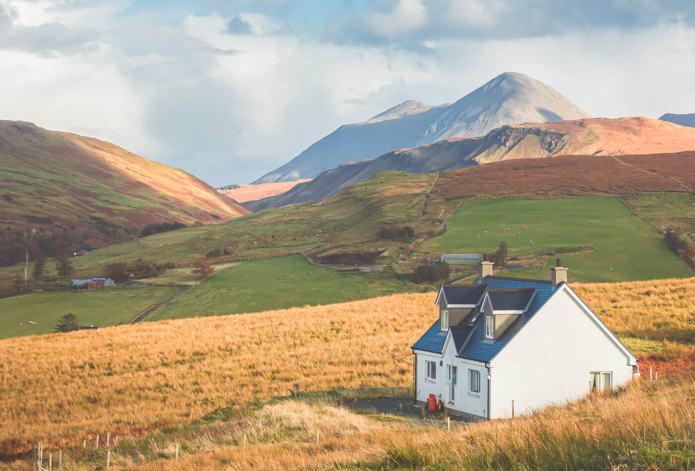 A white cottage sat in a field with mountain in the background on the isle of skye