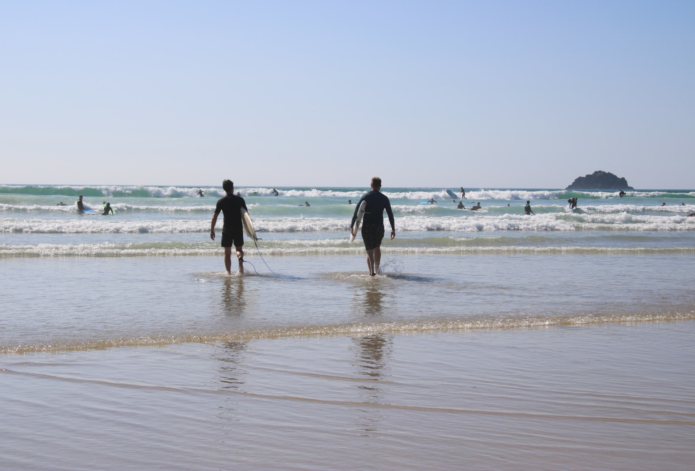 Two Surfers walking towards blue waves with surf boards in Polzeath, Cornwall