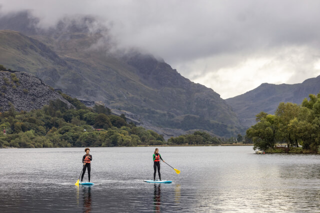 Two women paddle boarding Llyn Padarn