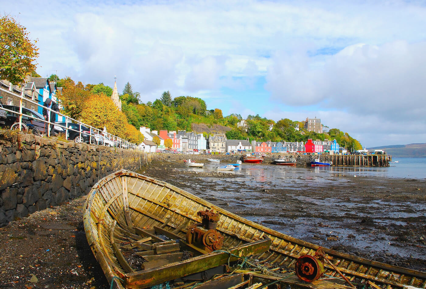 A derelict boat on the shore seen against a background of multi coloured houses in Tobermory on the Isle of Mull