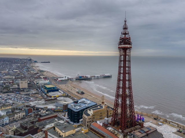 Close up of Blackpool Tower with city to the left and sea to the right on a cloudy day 