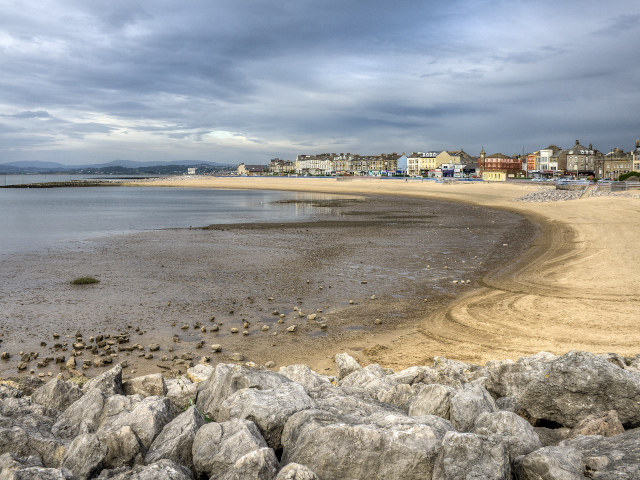 An overcast Morecambe Bay in Lancashire with sandy shores on the right and sea to the left, rocks in the foreground