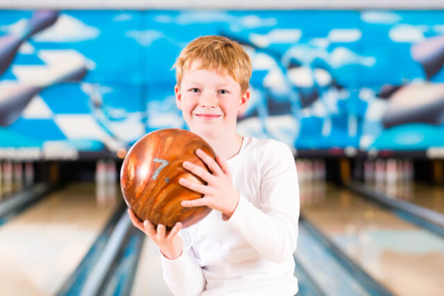young boy holding a bowling ball in a bowling alley