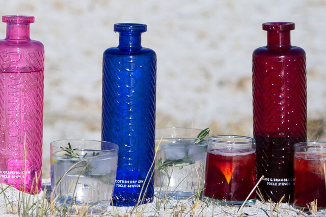 Three bottles of Downpour Gin on the beach