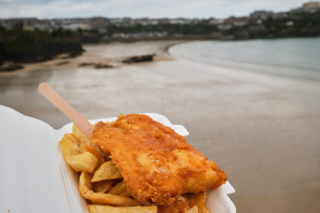 Fish and chips served in a tray in the foreground with grey coastal scenery in the background