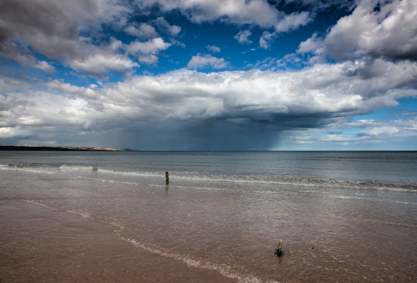 Quiet beach scene with gentle waves on the sand, blue skies and white clouds overhead