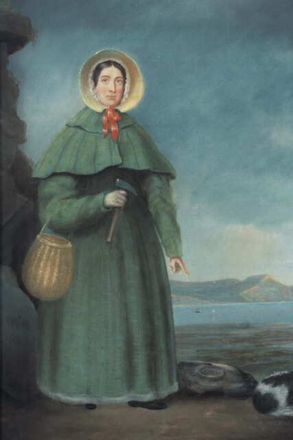 A painting of Mary Anning, a famous fossil hunter, standing on a beach in Dorset with her dog and pointing to a recently-found fossil on the ground.