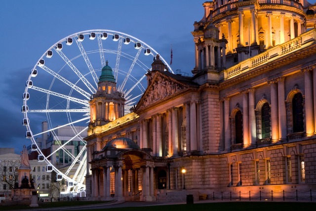 Belfast Christmas market with Ferris wheel beside City Hall illuminated at night.