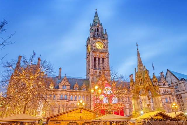 Manchester Christmas Market stalls with Town Hall and clock tower illuminated at night.