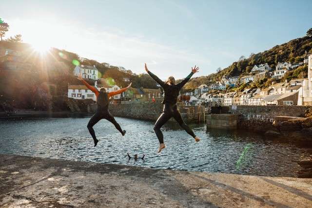 Two people in wet suits jumping into water.