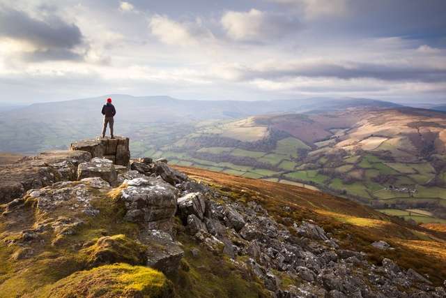 A person on the edge of a mountain overlooking the Brecon Beacon landscape surrounding.