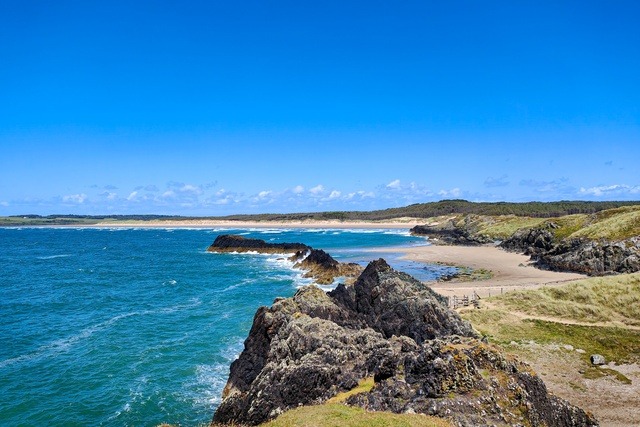Dramatic coastal cliffs and sandy beach along the Anglesey coastline in North Wales.
