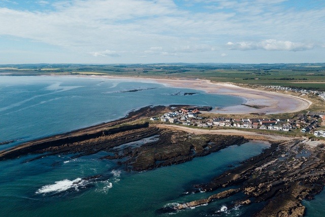 Wide sandy beach and rolling coastline at Beadnell Bay with clear blue sea.