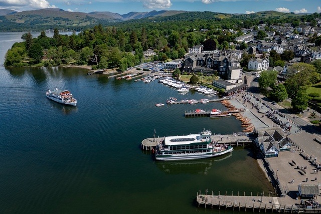 Scenic view of Bowness-on-Windermere marina with boats and Lake District hills in the background.