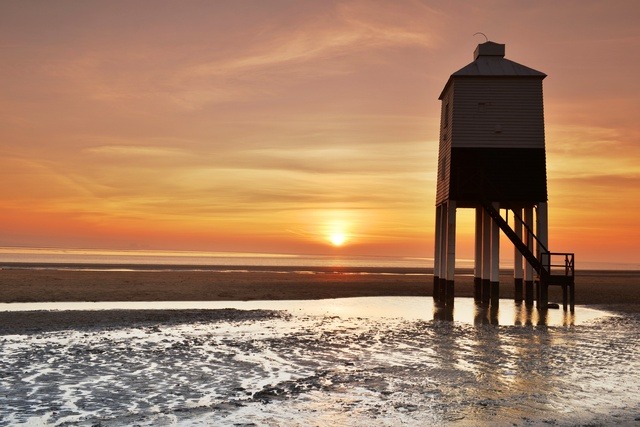 Burnham-on-Sea lighthouse standing on stilts at sunset with golden skies and wet sand reflections.