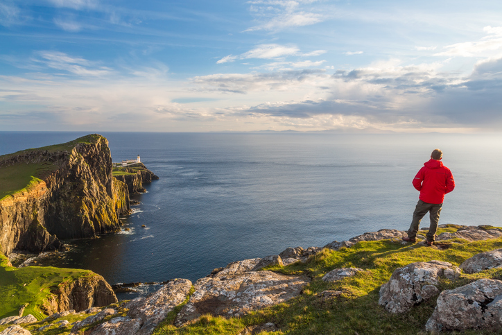 Man in red coat admiring the view, lighthouse in the Scottish highlands - an area that is ideal for a UK caravan escape.