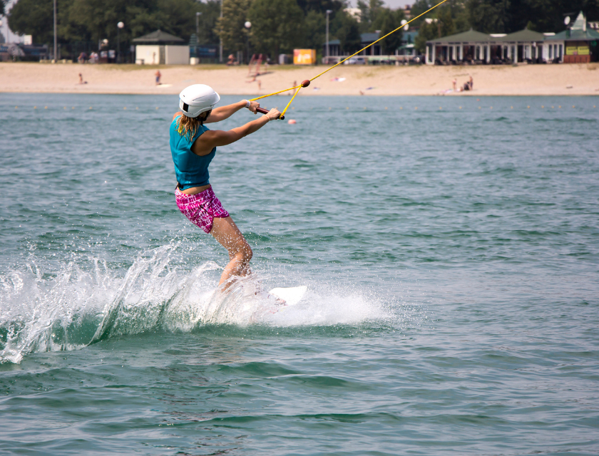 Shot from behind. Woman wearing a cap while kitesurfing with shoreline in the background.