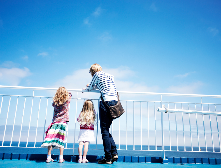 Woman and two children (two young girls) looking over a white fence. The light blue sky has several visible clouds.