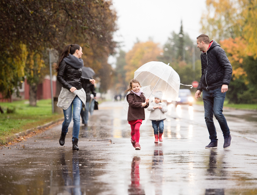 A father, mother and two children walking and smiling in the rain with umbrellas.