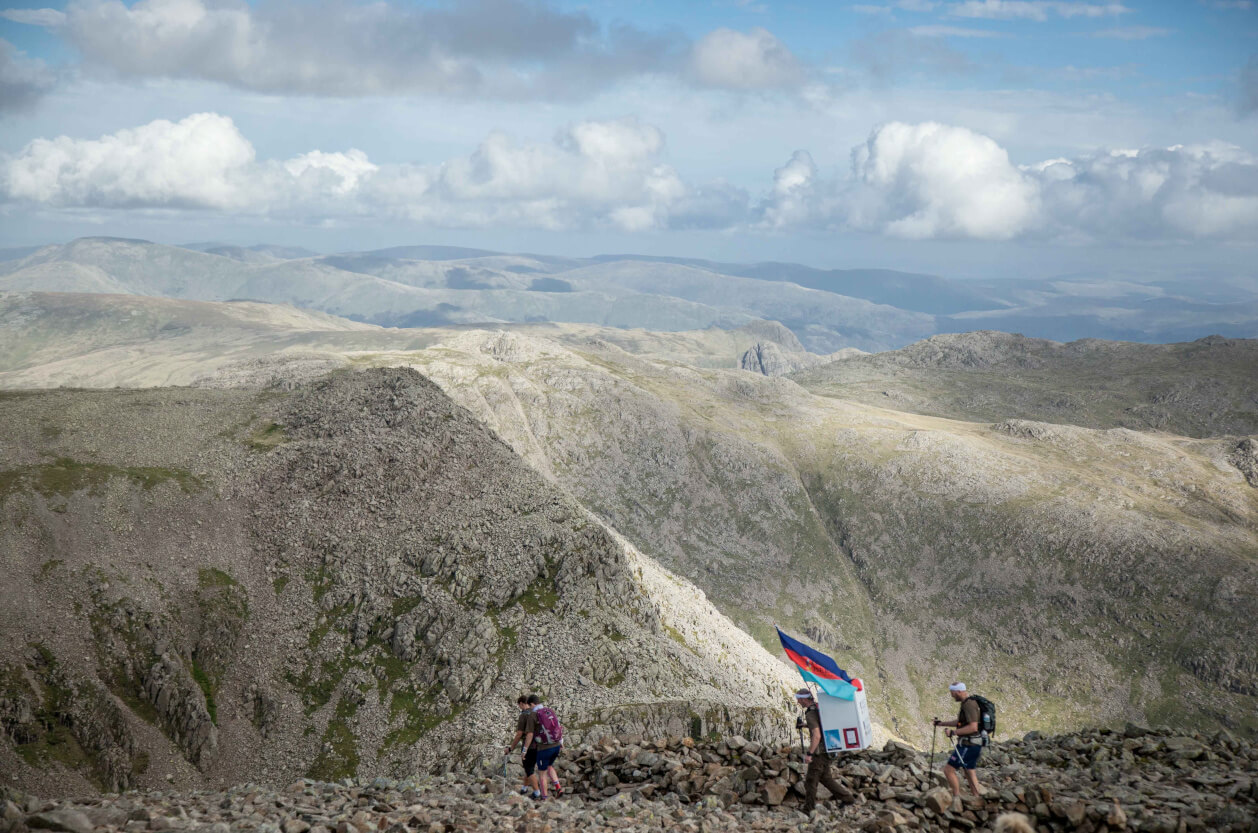 Small group of walkers on Scafell Pike with Lake District hills in background