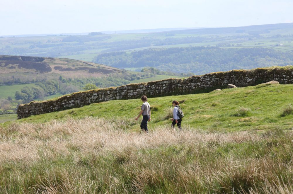 Two walkers walking alongside Hadrian's Wall on a summer's day