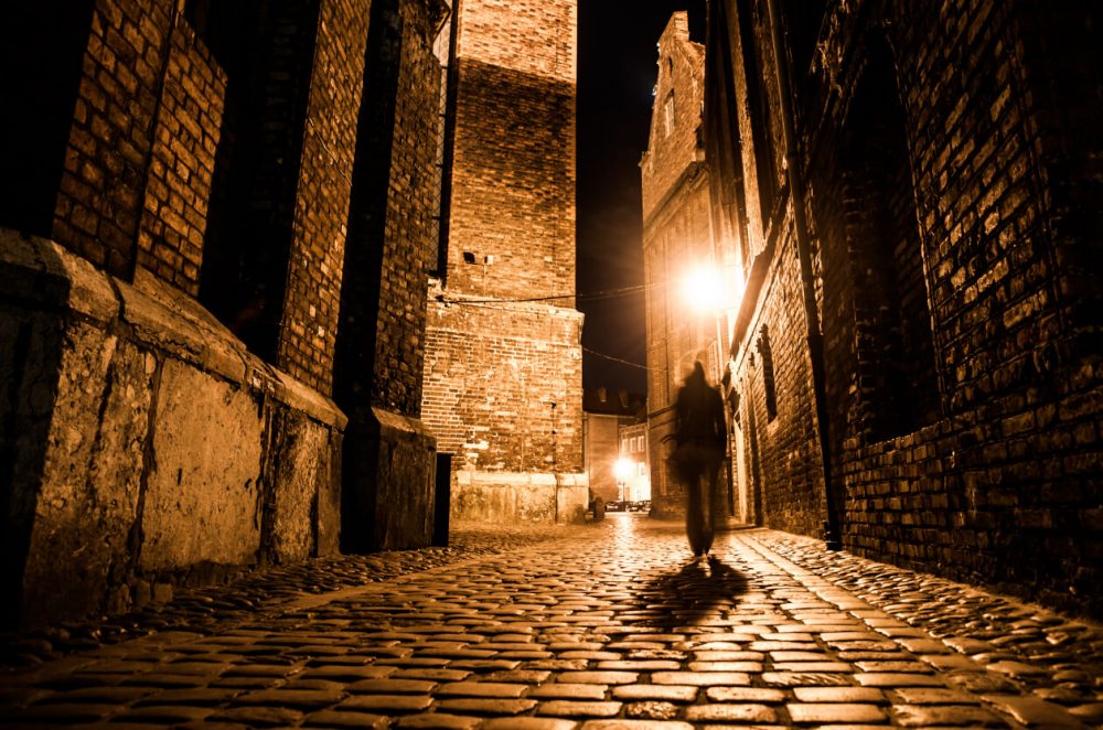 Shadowed figure walking up spooky alleyway at night