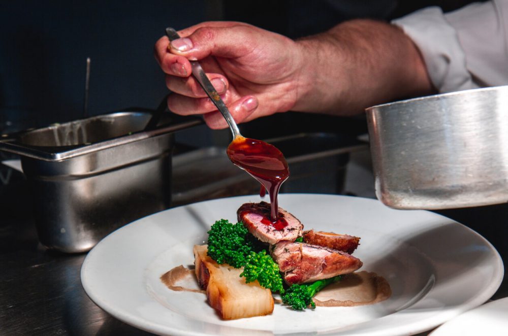 Chef pouring gravy over plate