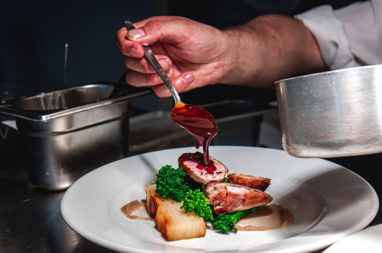Chef pouring gravy over plate