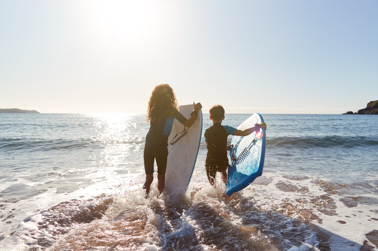 Two kids running into sea with bodyboards