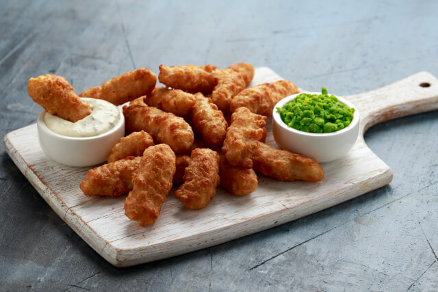 battered haddock on a board with mushy peas