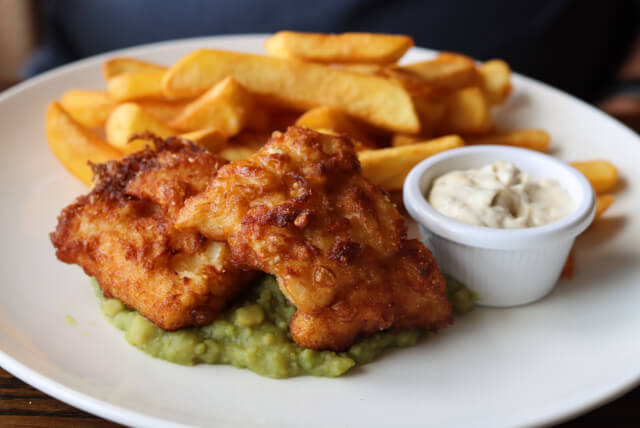 fish and chips atop mushy peas with tartar sauce