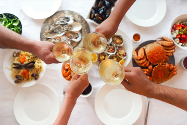 group clinking wine glasses over array of seafood dishes