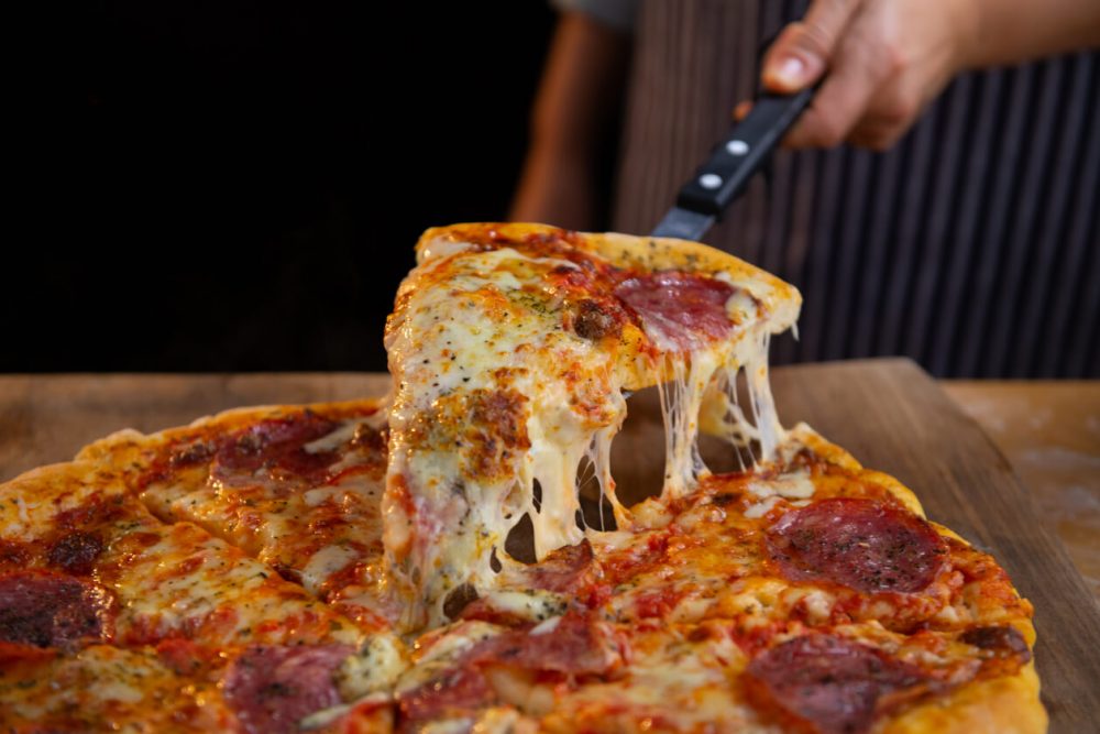 person lifting slice with a cheese pull from a pepproni pizza