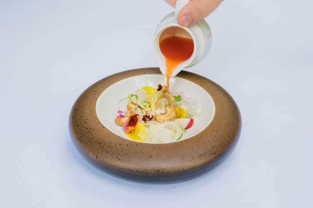 sauce being poured on michelin star dish