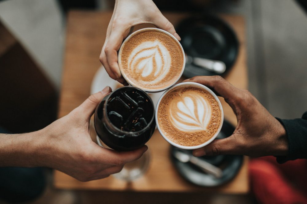 three people clinking coffee mugs