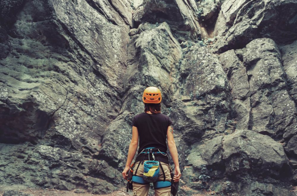 woman in rock climbing gear stood in front of a craggy mountain
