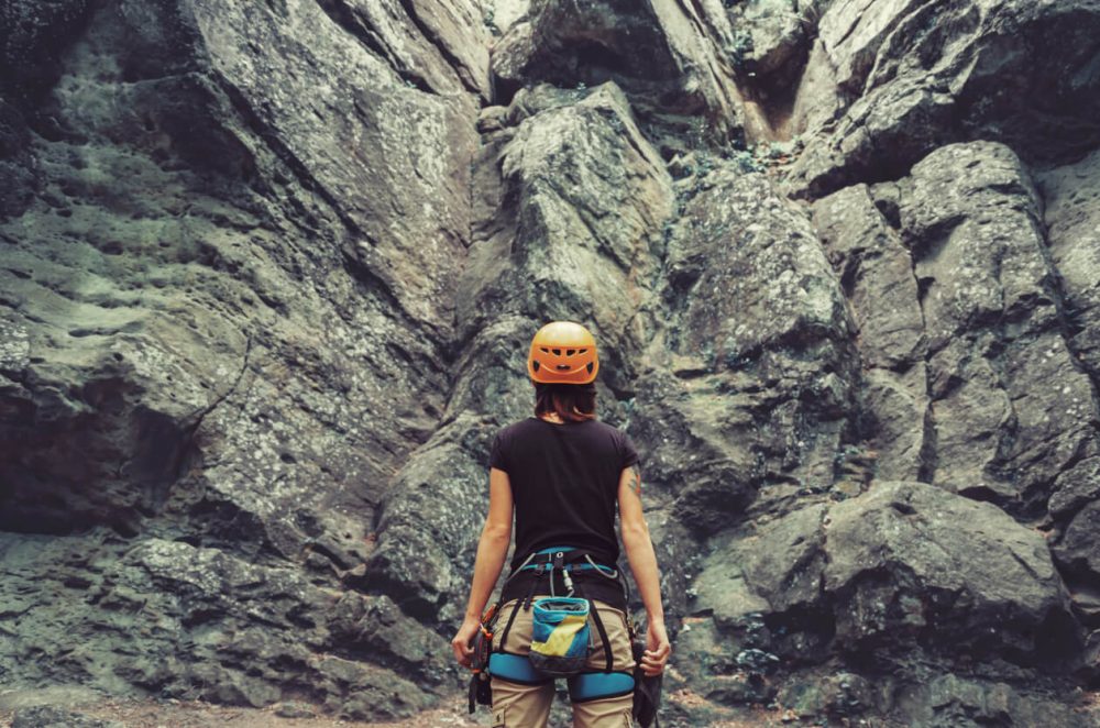 woman in rock climbing gear stood in front of a craggy mountain